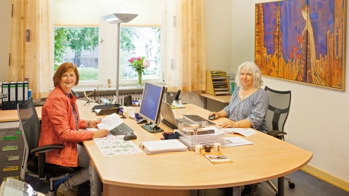 Zwei Frauen arbeiten in einem Büro an einem Tisch mit Computern