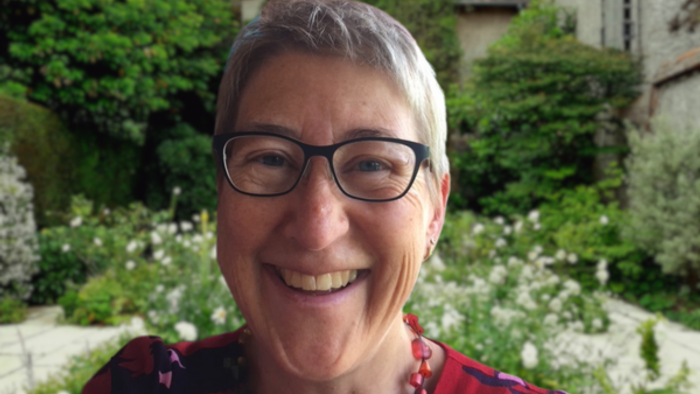 Eine Frau mit Brille lächelt in einem Garten.