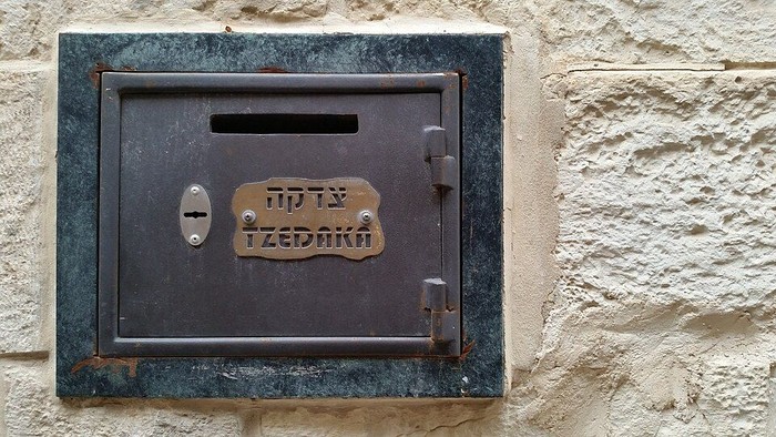 eine weiße Mauer mit eingelassenem Metall-Briefkasten mit dem Wort Tzedaka