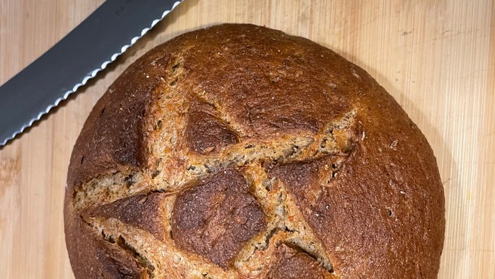Ein frisch gebackenes Brot liegt auf einem Schneidebrett neben einem Messer.