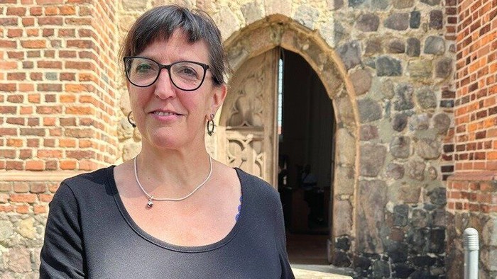Nicole Collier zeigt vor der St. Moritz-Kirche Mittenwalde einen Bauplan des Gebäudes.