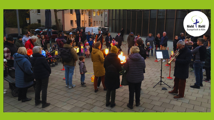 Menschen versammeln sich auf einem Kopfsteinpflasterplatz, einige halten Fackeln und Schilder.