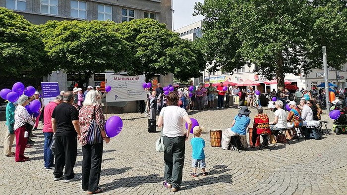 Auf dem Marktplatz stehen Menschen mit lila Luftballons im Kreis. Transparent der Mahnwache wird hochgehalten.