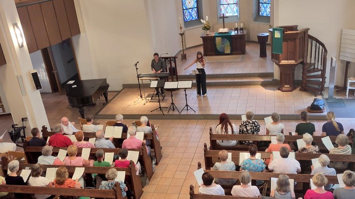 Eine Gruppe von Menschen sitzt in einer Kirche und hört einem Pianisten zu.