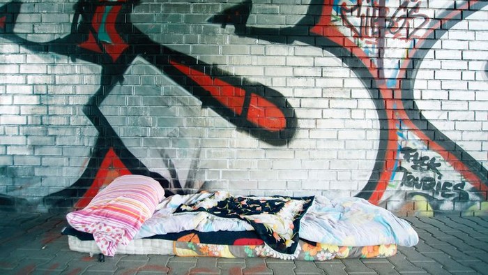 Ein Obdachloser schläft auf einer Decke vor einem Graffiti-Wand.