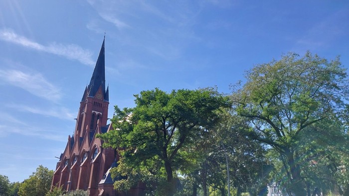 Die Kirche Zum Guten Hirten umgeben von Bäumen des Friedrich-Wilhelm-Platzes in Berlin Friedenau