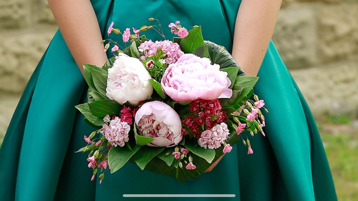 Eine Person in einem grünen Kleid hält einen Blumenstrauß mit rosa und weißen Blumen.
