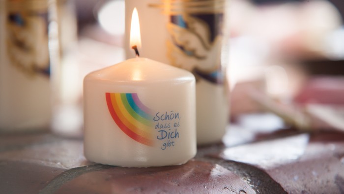 Weiße Kerze mit buntem Regenbogen und Aufschrift 