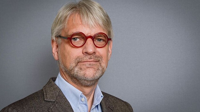 Mann mit blondem Haar und rotem Brillengestell, trägt Anzug und Krawatte