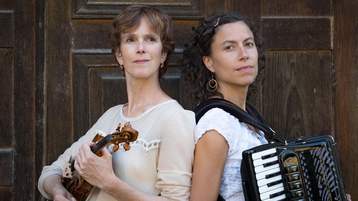 Zwei Frauen mit Musikinstrumenten vor Holztür