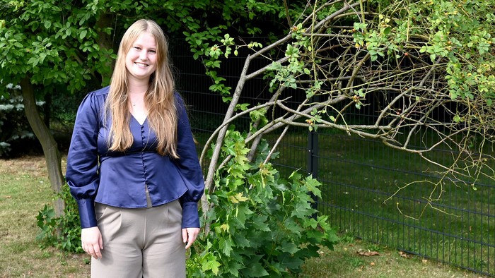 Eine junge Frau steht im Freien vor einem Baum und lächelt.