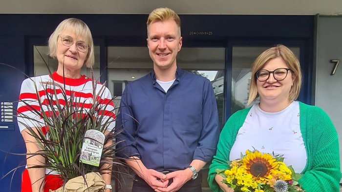 Drei Personen halten Blumensträuße und posieren für ein Foto