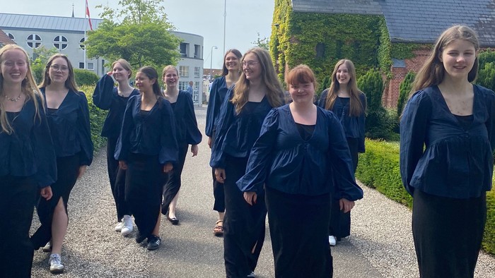 En gruppe af studerende i færdselsmørke går i procession forbi en kirke.