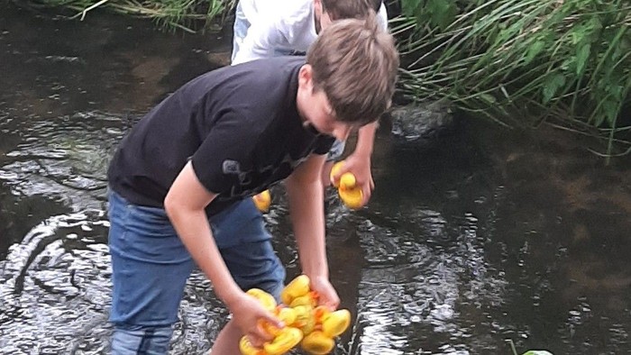 Zwei Jungen spielen mit gelben Enten in einem Bach.
