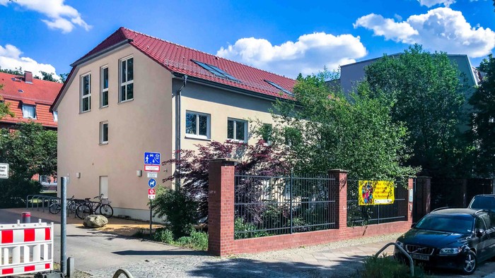 Haus mit rotem Dach und Garten, Auto und Fahrrad auf Straße, blauer Himmel