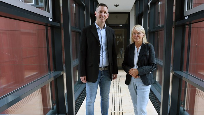 Zwei Personen stehen in einem modernen Gebäude mit Glaswänden.