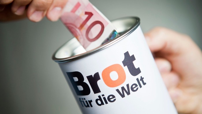 Ein Geldschein wird in eine Spendendose von Brot für die Welt gesteckt