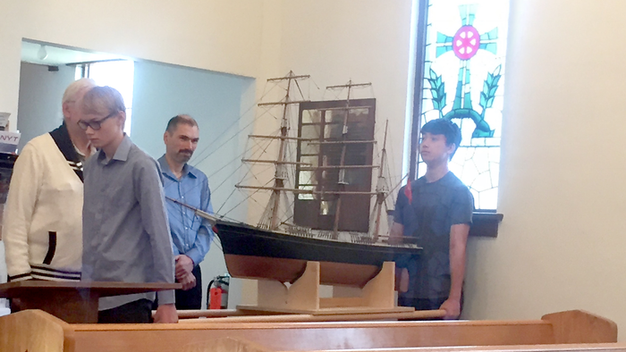 Three men in church examining model ship.