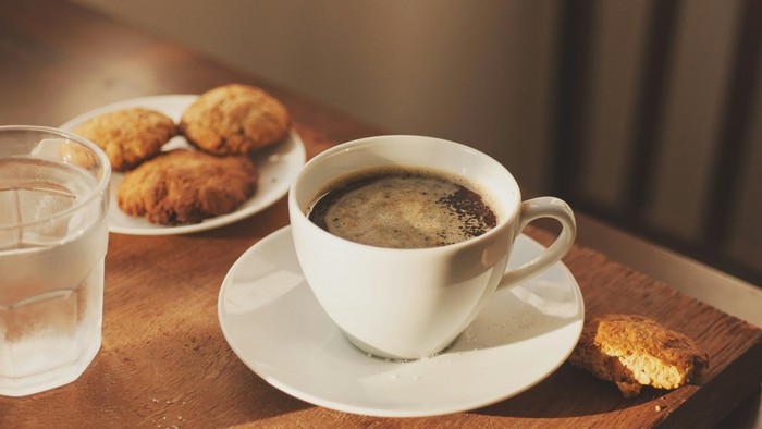 En kaffekop og en drikkeglans på en bord med kager og en småkage.