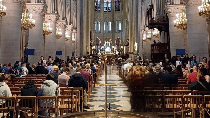 Große Kirche mit vielen Menschen, die auf Bänken sitzen und Kerzenleuchter an den Wänden