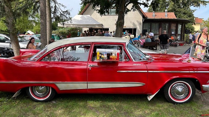 Ein rotes Oldtimer-Auto auf einem grasbewachsenen Bereich bei einer Veranstaltung.