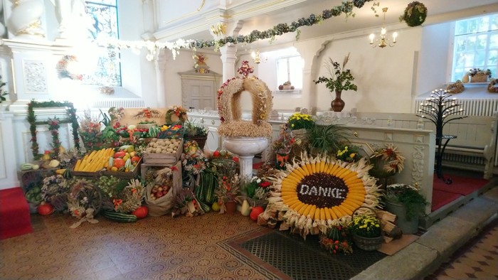 Ein festlich geschmückter Raum mit Blumen und Kränzen, ein großes Dankes-Sonnrad im Vordergrund
