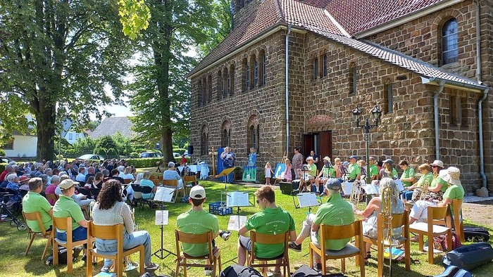 Eine Gruppe von Menschen singt vor einem alten Steinhaus im Freien.