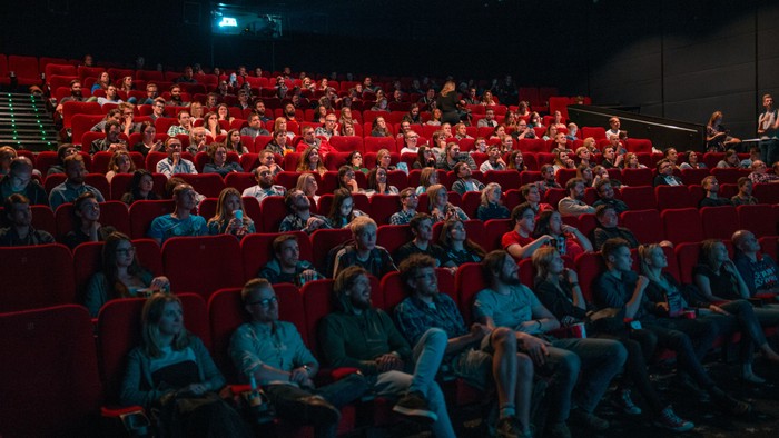 Ein volles Kino mit vielen Menschen auf roten Sitzen.