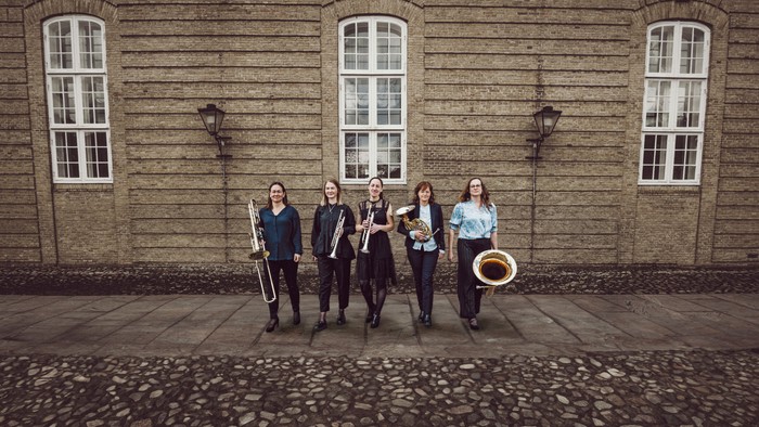 En gruppe musikere står med instrumenter forud for et gammelt stenhus.