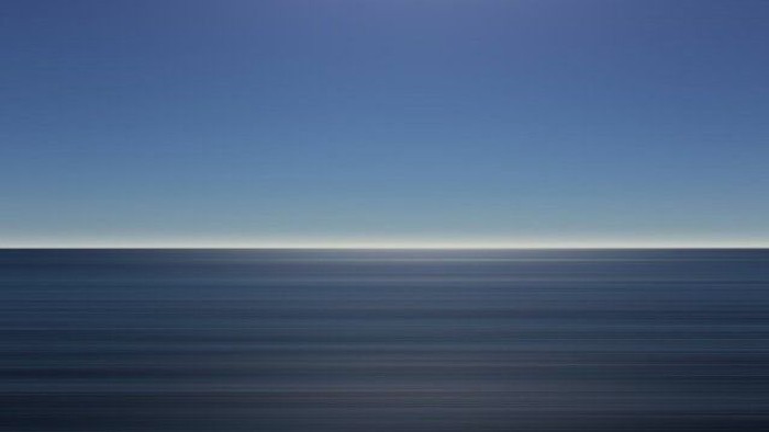 Ein ruhiges Meer bei Dämmerung mit dunklem Horizont und hellblauem Himmel.