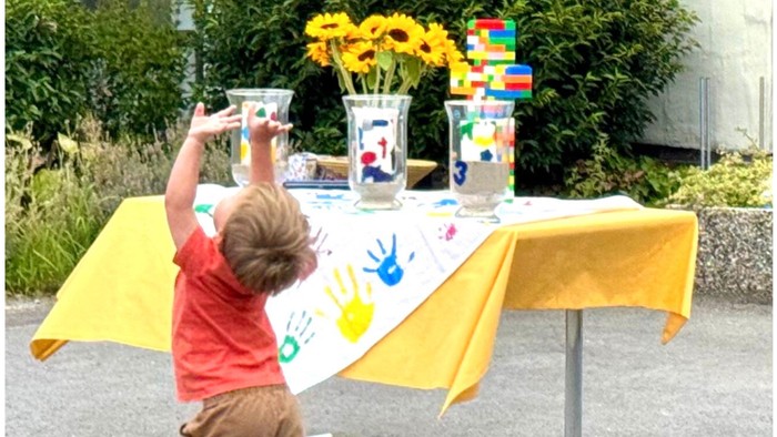 Kind spielt mit einer Spielzeugkamera an einem Stand mit Blumen und bunten Dosen