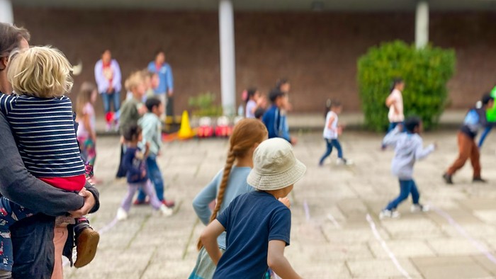 Mehrere Kinder spielen auf einem Platz. Links wird ein Kind auf dem Arm gehalten.
