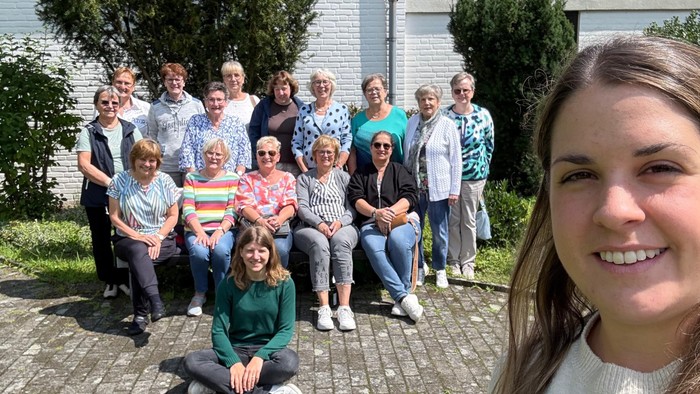 Gruppe von Menschen vor weißem Haus auf Rasen und Kopfsteinpflaster