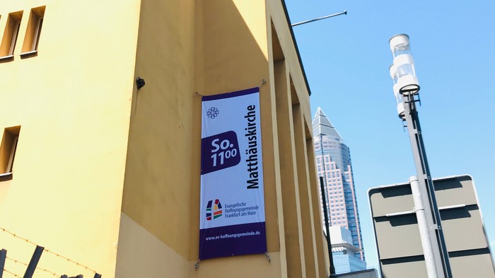 Gelbe Gebäudeecke mit Werbung für Mathematikwoche und Skyline im Hintergrund