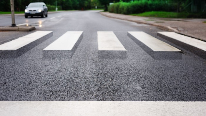 Ein Zebrastreifen auf einer Straße mit einem Auto im Hintergrund.