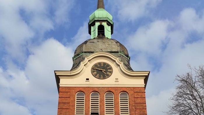 Der Kirchturm hat ein grünes Dach und eine Uhr.