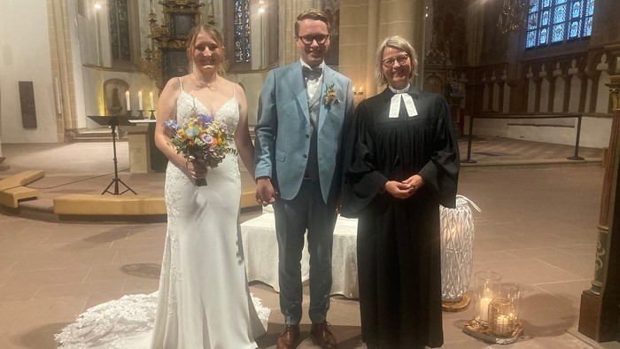 Ein Brautpaar posiert mit dem Pfarrer in einer Kirche