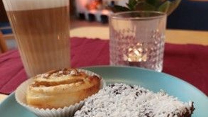 Auf dem Tisch stehen ein Glas Milch, ein Kuchenstück und eine Tasse mit Gebäck.