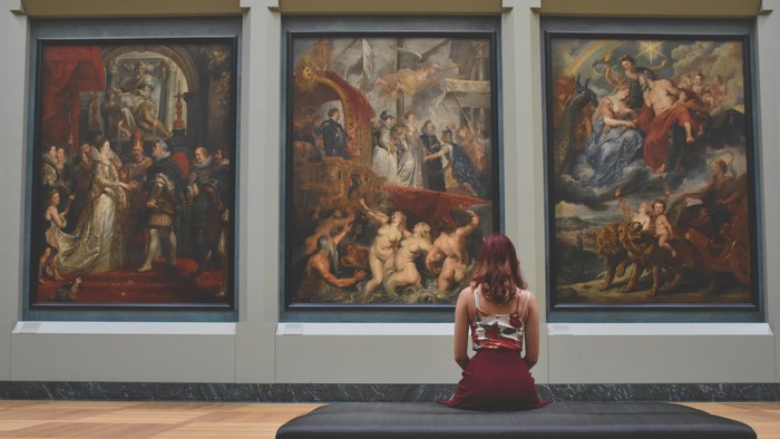 Frau sitzt auf Bank und schaut drei große Gemälde in Museum