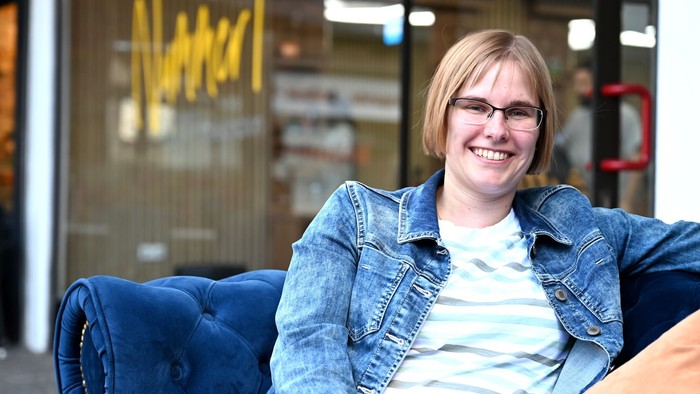 Eine Frau sitzt in einem blauen Sessel und lächelt.