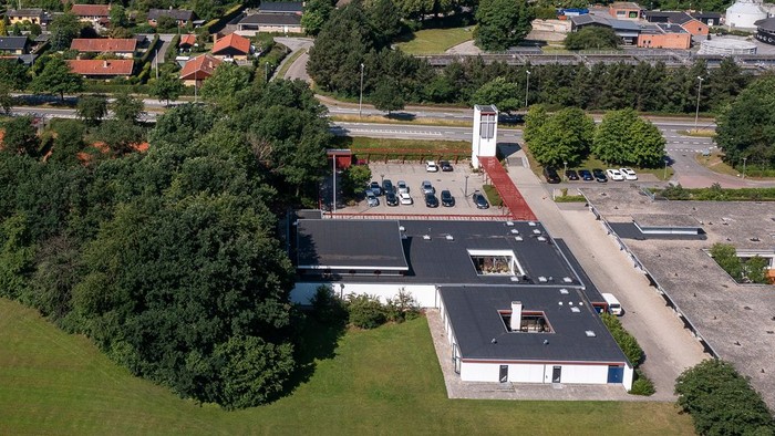 En stor industrikompleks med en høj røgkamin i en by omgivet af grønne områder.
