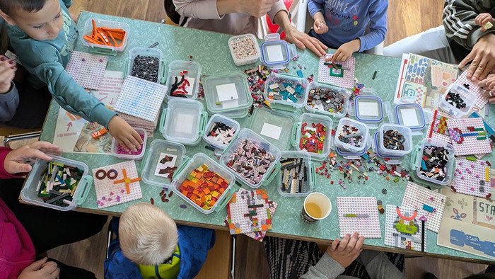 Tisch von oben voller bunter Legosteine in Behältern und Kinder am Basteln