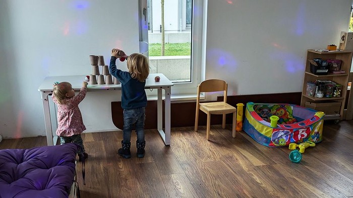 Zwei Kinder stapeln Becher auf einem Tisch. Weitere Spielgeräte im Raum.
