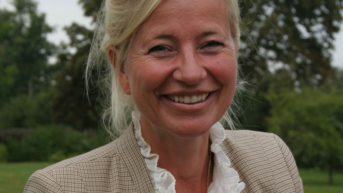 En kvinde med blond hår og en blå blazer smiler til kameraet.