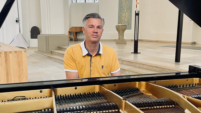 Popkantor Sven Bergmann spielt den Flügel in der Johanniskirche. Er trägt ein gelbes Polo-Shirt und lächelt in die Kamera.