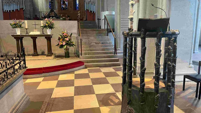 In der Kirche steht ein Pult auf einem Schachbrettboden, umgeben von Blumen und Stufen.