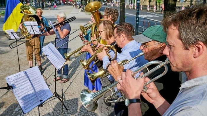 Mehrere Menschen, die Trompete, Tuba und Posaune spielen. Ukrainische Flagge im Hintergrund.