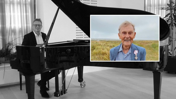 En mand spiller piano med et billede af en anden mand viset på skærmen.