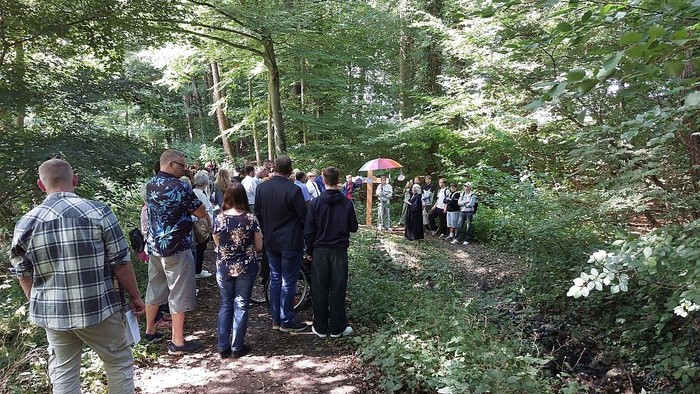 Eine Gruppe von Menschen steht im Wald und hört einem Redner zu.
