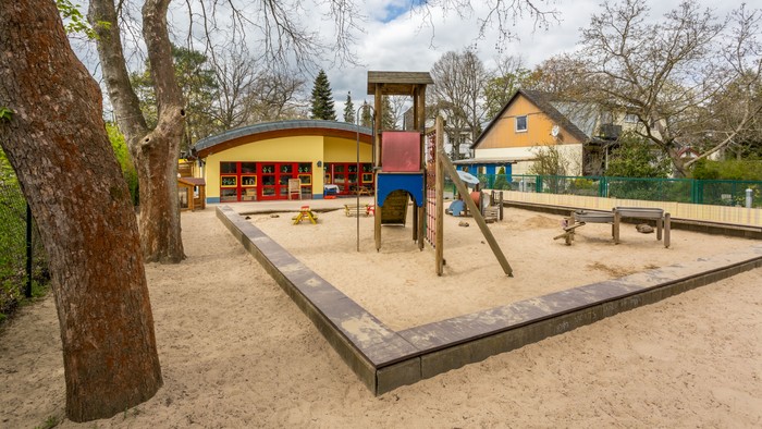 Ein Spielplatz mit Sandkasten und Klettergerüst vor einem farbenfrohen Gebäude.